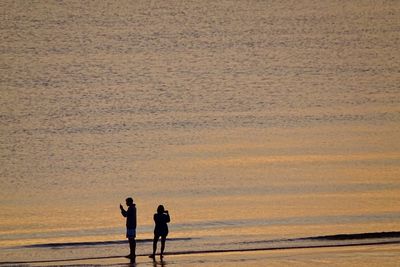 Rear view of people walking at beach against sky during sunset