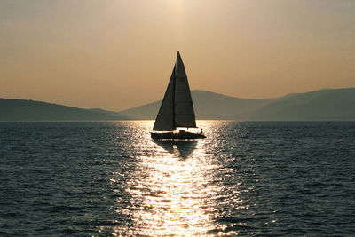 Silhouette sailboat sailing on sea against sky during sunset