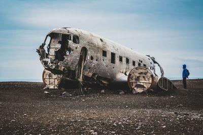 Man looking at abandoned airplane on field against sky