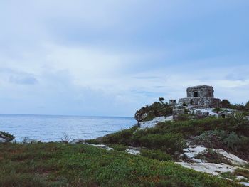 Old ruins by sea against cloudy sky
