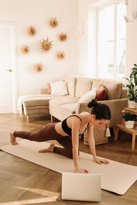 Fitness girl looks at her laptop while doing sports training and physical activity at home