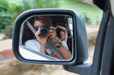 Portrait of woman photographing camera on side-view mirror