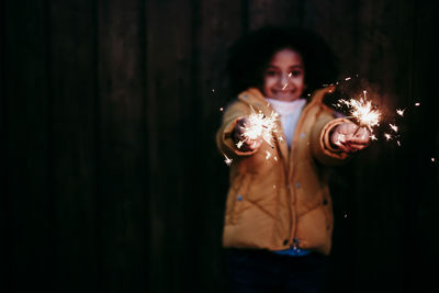 Girl standing and holding burning sparkler at night