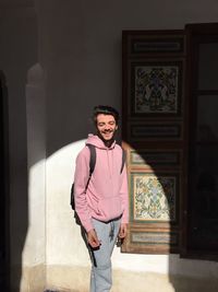 Portrait of smiling young woman standing against wall