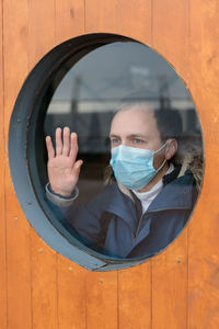Man wearing mask while looking through window