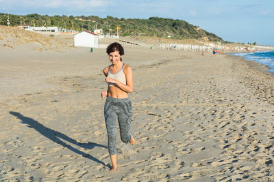 Young woman running at beach against blue sky