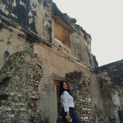 Portrait of woman standing by building against sky