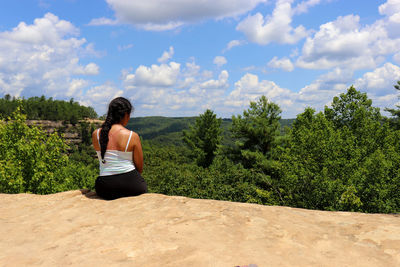 Rear view of woman standing on rock against sky