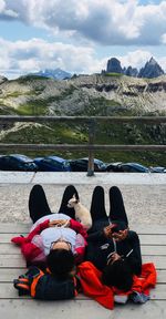 Rear view of people sitting on mountain against sky