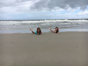 Sisters lying at beach against cloudy sky