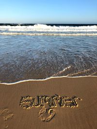 Text on sand at beach against sky