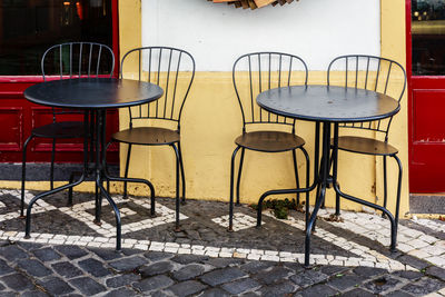 Empty chairs and tables at sidewalk cafe against building