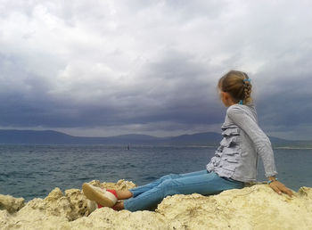 Side view of girl looking at lake against cloudy sky