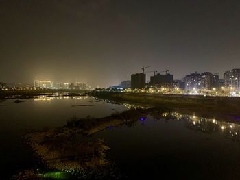 Illuminated buildings by river against sky at night