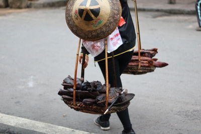 Low section of woman carrying meat in baskets on street for sale