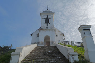 Low angle view of cross amidst buildings against sky