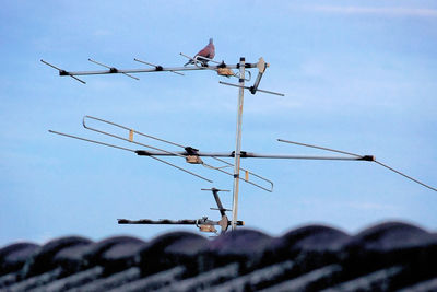 Low angle view of bird perching on antenna against sky