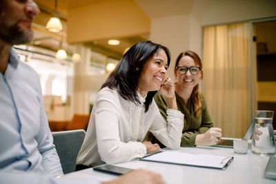 Cheerful businesswomen sitting at conference table during sales meeting in office