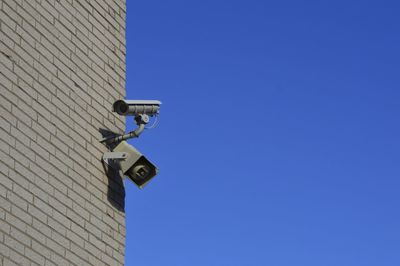 Low angle view of surveillance camera against clear blue sky