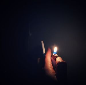 Midsection of person holding lit candle in darkroom