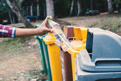 Cropped hand of man putting bottle in garbage bin