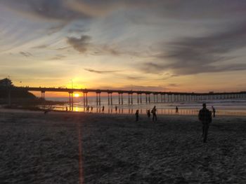 Silhouette people walking on beach against sky during sunset