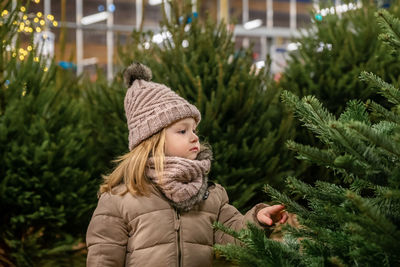 Small girl chooses a christmas tree in the market.