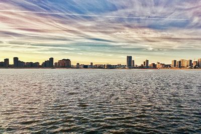 Sea by buildings in city against sky at sunset