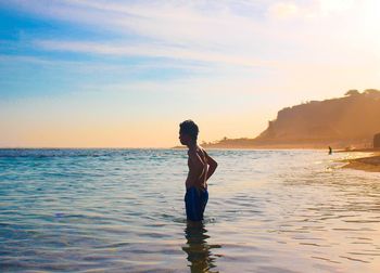 Woman in sea against sky during sunset