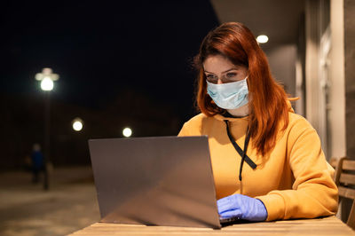 Businesswoman wearing mask using laptop in cafe at night