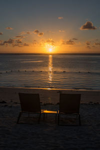 Chairs on beach against sky during sunset