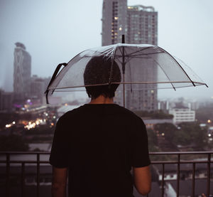 Rear view of man standing against cityscape during rain