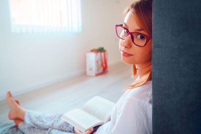 Portrait of woman wearing eyeglasses reading book at home