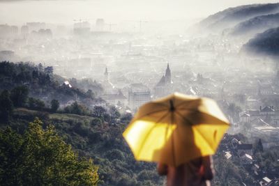 Rear view of man with umbrella against buildings in city