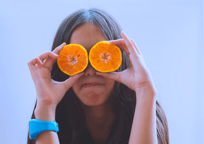 Close-up of girl holding orange slices against clear sky