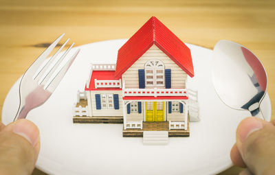 Cropped hands of person holding cutlery with model home in plate on table