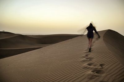 Rear view of man walking on sand dune