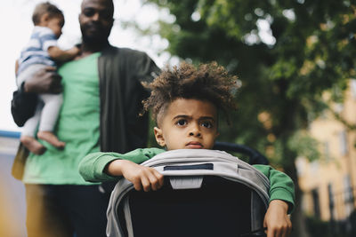 Boy in baby stroller with father and brother in background