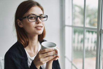 Portrait of young woman drinking coffee by window