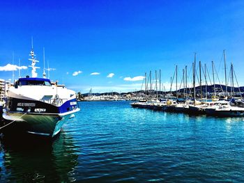 Boats moored at harbor against blue sky