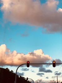 Low angle view of street lights against cloudy sky