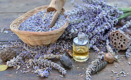 Lavender flowers petals in a little basket with essential oil bottle on a wooden table