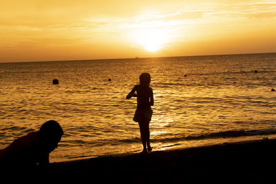 Silhouette woman on beach against sky during sunset