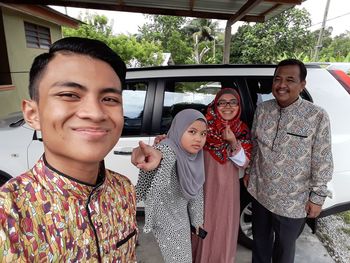 Portrait of smiling family standing against car