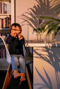 Cute happy toddler boy playing hide and seek hiding his face behind hands in hard sunset  light.