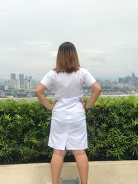 Rear view of woman standing with hand on hip by plants at terrace