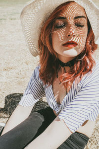 Young woman wearing hat with eyes closed sitting on field