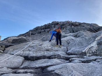 Low angle view of woman climbing on rock against sky