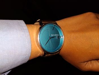 Close-up of hand holding clock against black background