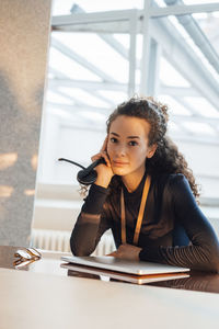 Young customer service representative sitting with headset and laptop at desk in office